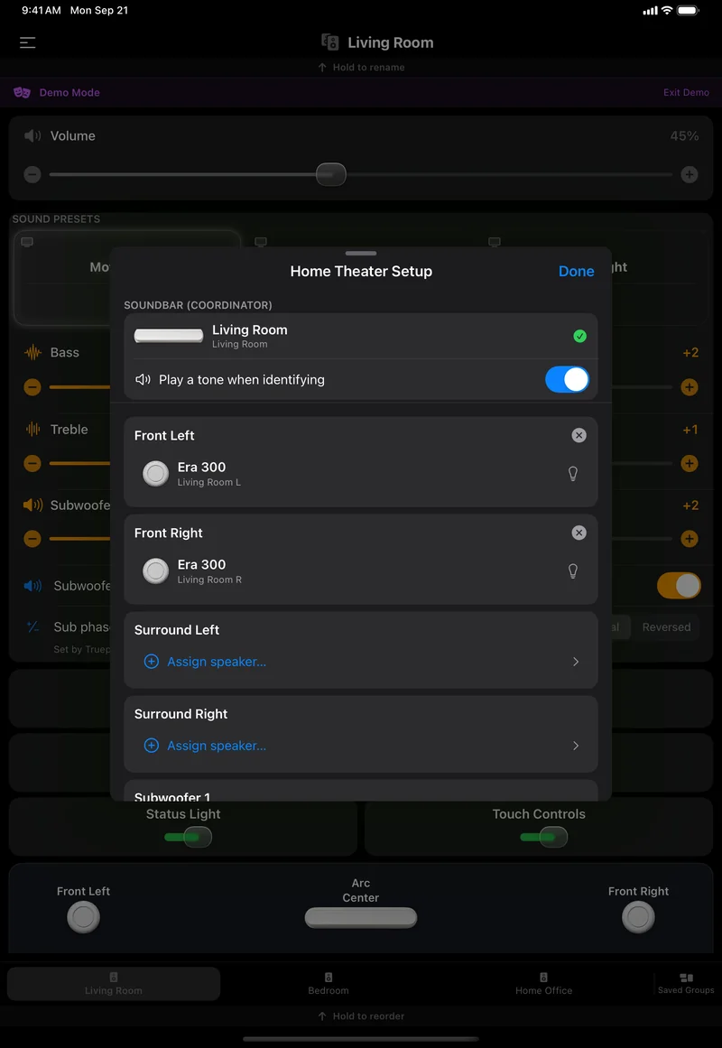 The Home Theater Setup sheet centred over the Living Room page on an iPad: Living Room as the soundbar coordinator, Play a tone when identifying on, Era 300 in Front Left and Front Right with bulb and remove buttons, and Assign speaker rows for Surround Left, Surround Right and Subwoofer 1.